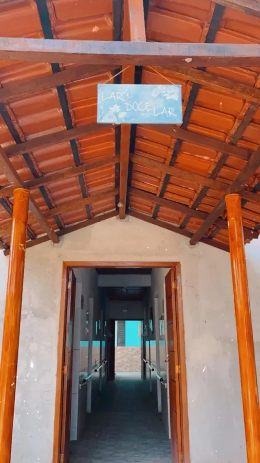 Entrada da casa, com telhado de telhas aparentes e placa escrita Lar Doce Lar